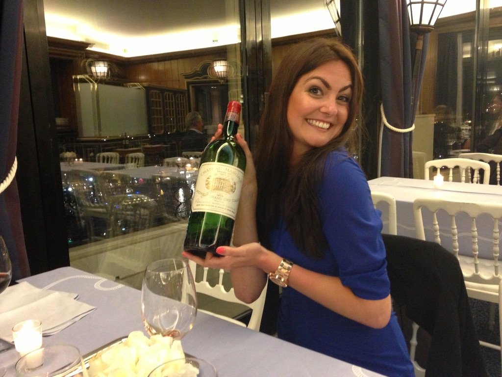 Charlotte Sapak smiling at dinner holding a bottle of Château Margaux